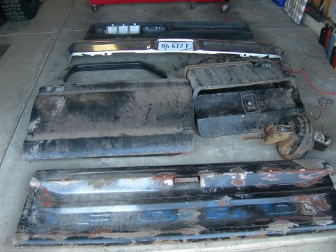 1985 Ford Bronco - Various disassembled truck parts are laid out on a concrete floor, including a tailgate with visible lettering.