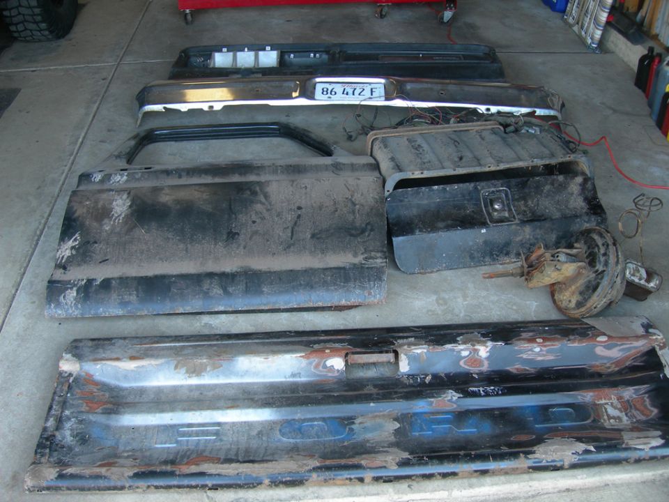 Truck bed, tailgate, bumper, and fuel tank laid out on a garage floor. License plate reads 86 472 F