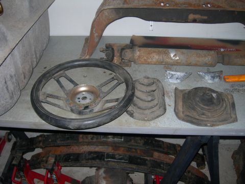 1985 Ford Bronco - Various vehicle parts, including a steering wheel and leaf springs, are laid out on a table.