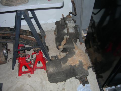1985 Ford Bronco - Transfer case and leaf springs are shown supported by red jack stands, with a portion of a black vehicle visible on the right.
