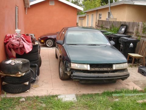 1995 Ford Taurus - Front view of a damaged 1995 Ford Taurus parked in a driveway with another car.