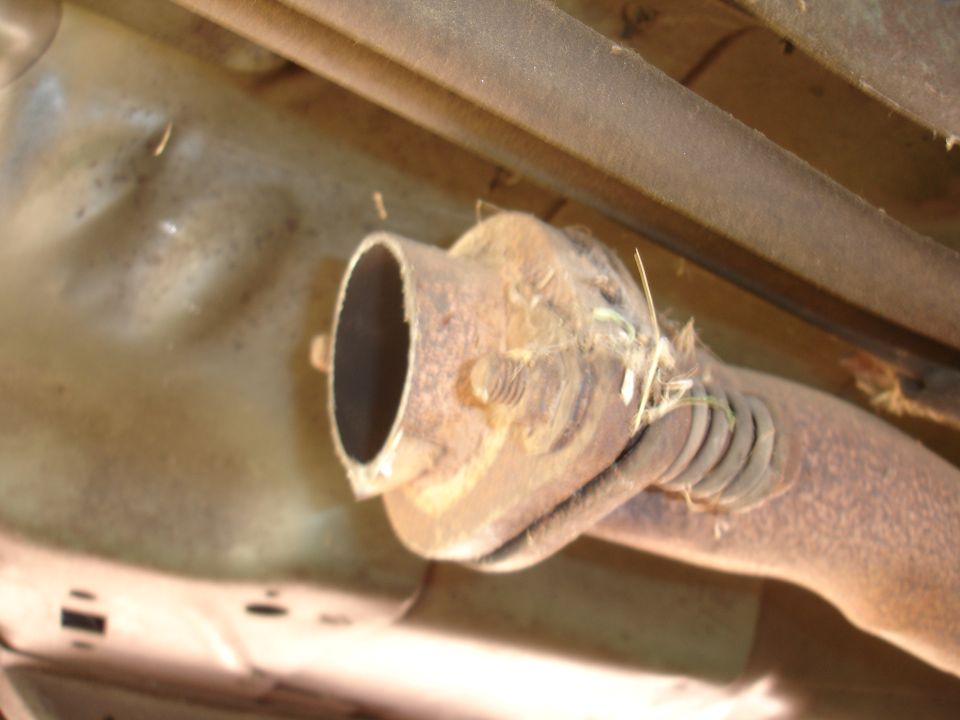 Exhaust pipe with rust and debris, viewed from underneath a vehicle