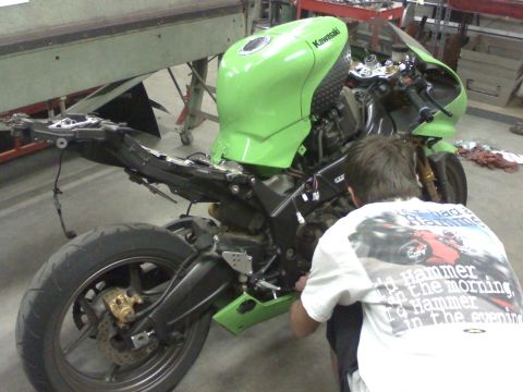 2005 Kawasaki Ninja R - A person works on a green 2005 Kawasaki Ninja R motorcycle in a workshop setting.