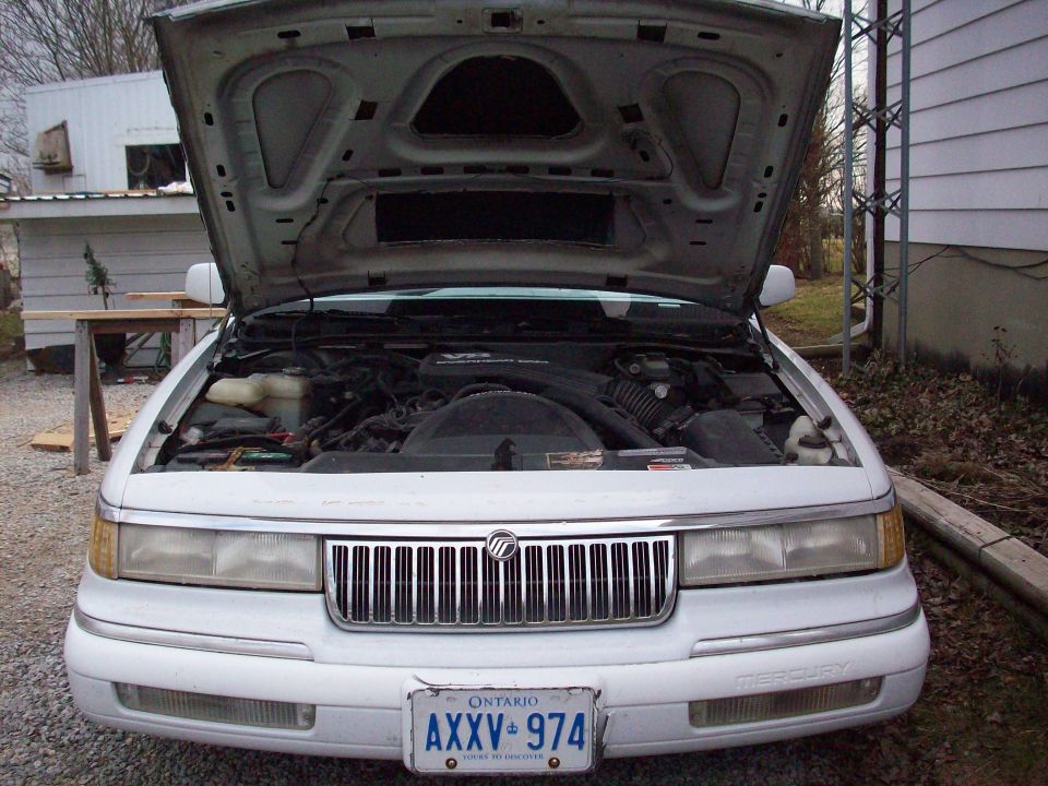 White Mercury sedan with hood up showing engine, Ontario plate AXXV 974, parked on gravel