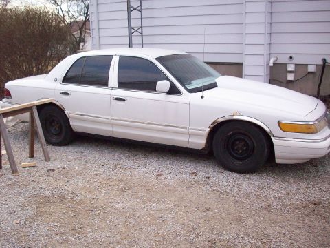 1992 Mercury Grand Marquis - A white 1992 Mercury Grand Marquis is parked on a gravel lot next to a white building.