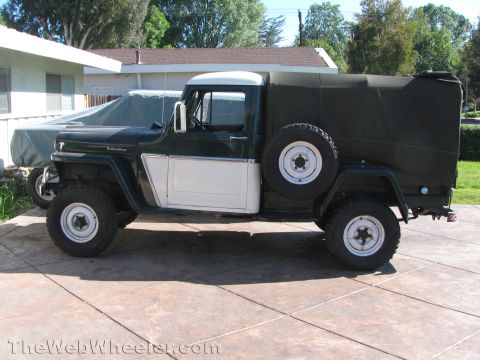 1968 Ford Mustang - A vintage Jeep truck with a canvas bed cover is parked on a concrete driveway next to a covered vehicle.