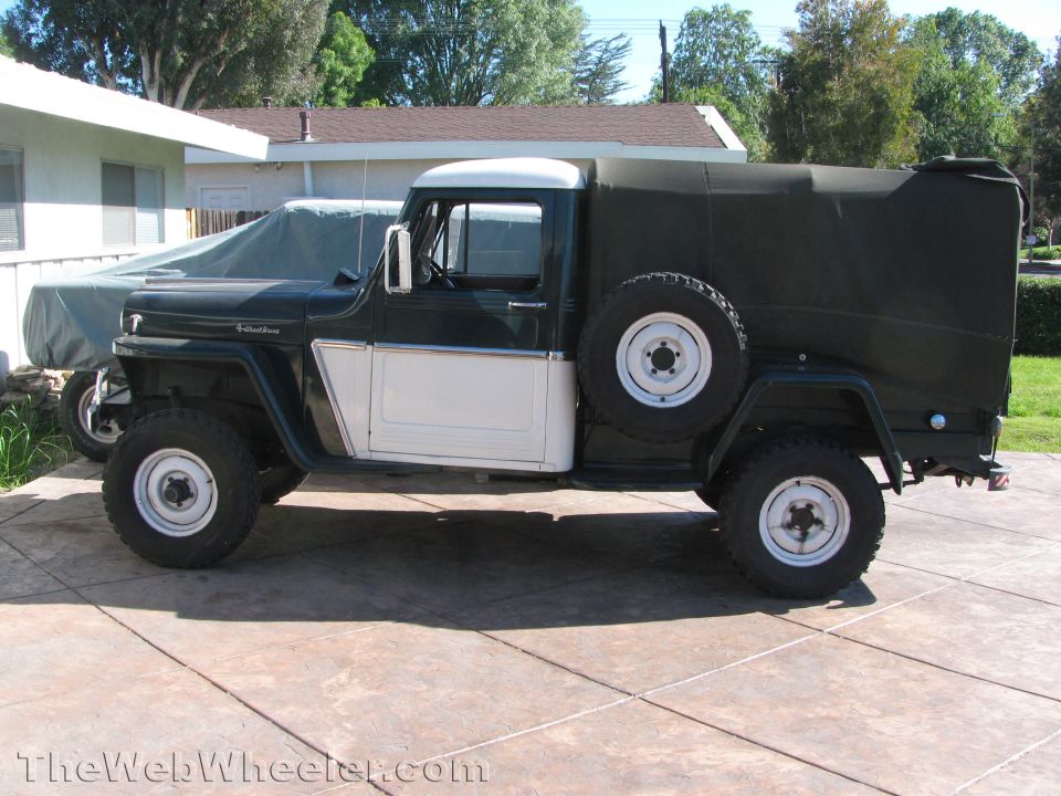 Green and white Jeep truck with a spare tire mounted on the side, parked on a concrete driveway