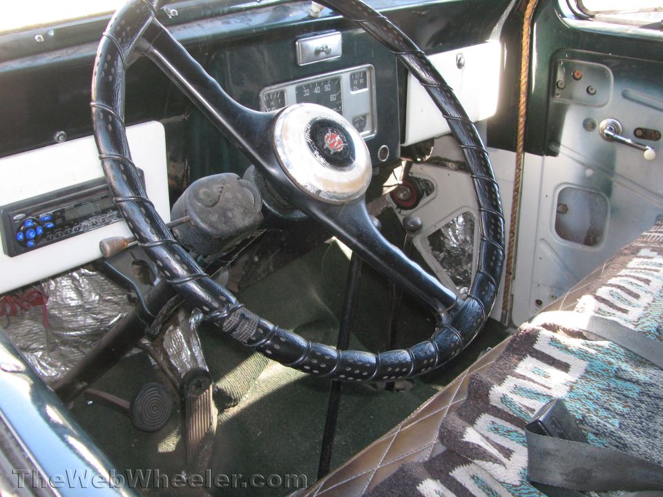 Interior view of a vintage vehicle's dashboard and steering wheel with a patterned seat cover