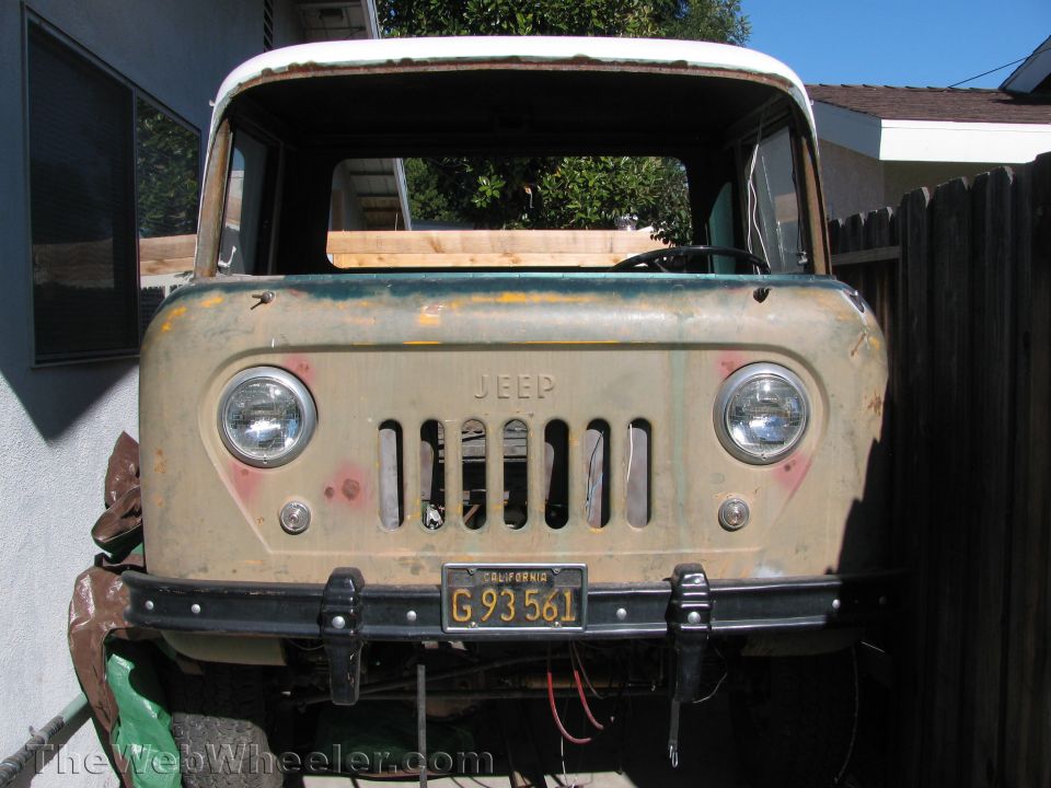 Front view of an old Jeep truck with a faded tan body and a white roof. It has a vertical grille and round headlights. California license plate G 93 561 is visible