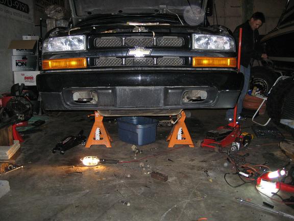 Black Chevrolet Blazer on orange jack stands in a cluttered garage, front view