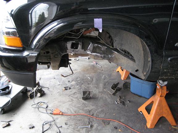 2004 Chevrolet Blazer front wheel well area with suspension disassembled, supported by jack stands