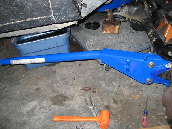 Blue suspension part with 'James Dun' sticker, under a vehicle with oil pan