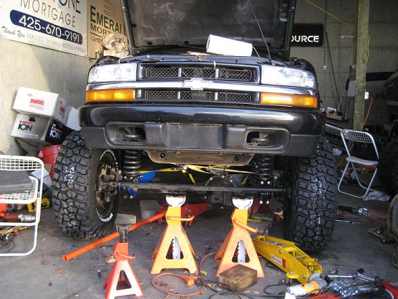 Black Chevrolet Blazer on jack stands showing lifted front suspension in a garage