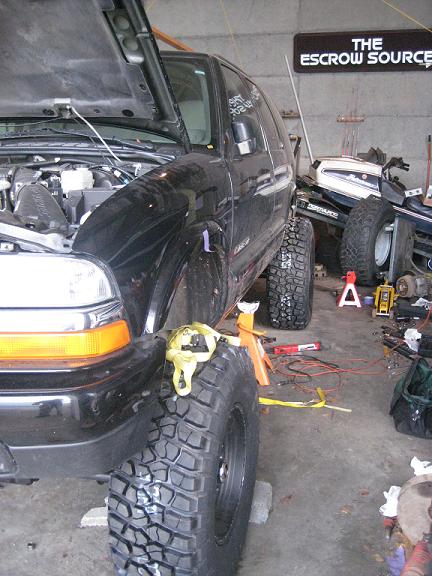 2004 Chevrolet Blazer - A black 2004 Chevrolet Blazer is shown in a garage with its hood up and lifted on jacks, displaying its off-road tires.