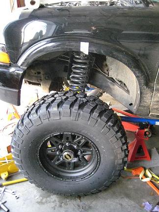 2004 Chevrolet Blazer - A large off-road tire and suspension components are visible on a vehicle being worked on.