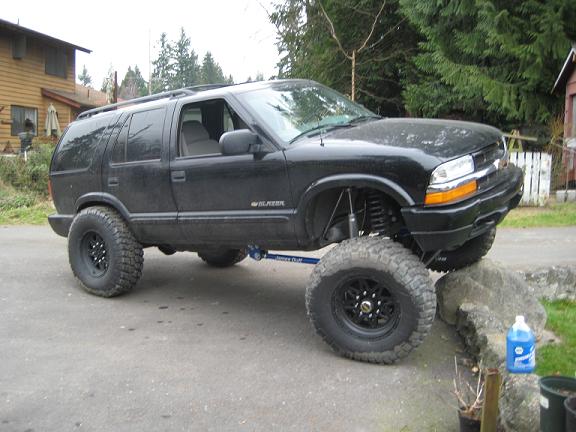 Lifted black Chevrolet Blazer flexing front tire up onto rock ledge in driveway