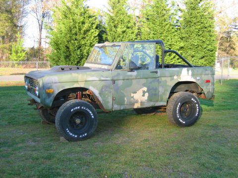 1992 Ford Mustang - Driver-side profile of a green camouflage early Ford Bronco parked on a grass yard with the doors, top and fenders removed, exposing red co…