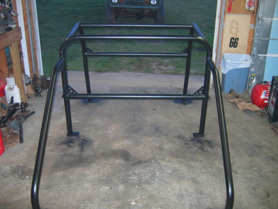 Black metal roll cage with four horizontal bars and two vertical supports, mounted on a concrete floor