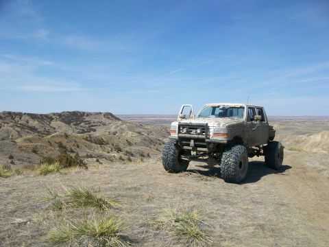 1992 Ford F-350 - This lifted 1992 Ford F-350 is shown off-road in a dry, hilly landscape under a clear blue sky.