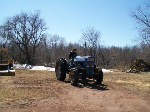 2000 Chevrolet Tahoe - A blue tractor is being driven across a rural landscape under a clear blue sky.
