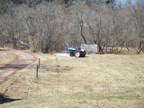 2000 Chevrolet Tahoe - A blue tractor sits in a field with bare trees in the background and a dirt road curving to the left.