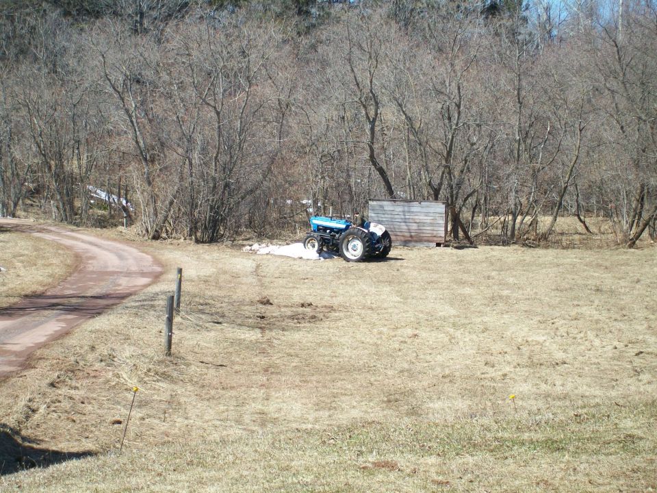 Blue tractor parked in a dry, grassy field next to a wooden shed