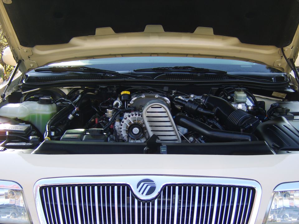 Engine bay of a Mercury showing supercharged V8 with hood open and chrome grille below