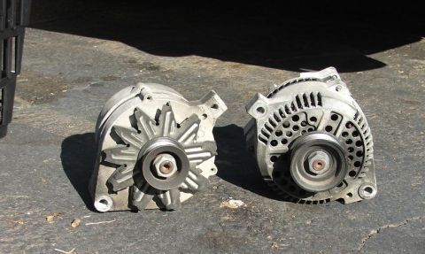 1985 Ford Crown Victoria LTD - Two automotive alternators are shown side-by-side on a paved surface, with a watermark for Supermotors.net visible.