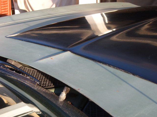 Car hood with a black scoop and part of the windshield wipers visible