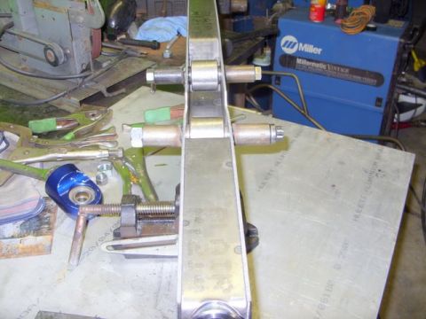 2008 Ford Bronco - A metal suspension part is clamped down on a workbench, surrounded by various tools and equipment in a workshop setting.