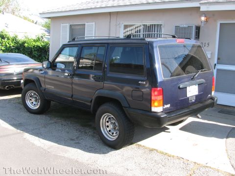 1987 Suzuki Samurai - Photo of a dark blue Jeep Cherokee XJ 4x4 parked in a residential driveway, rear three-quarter view.