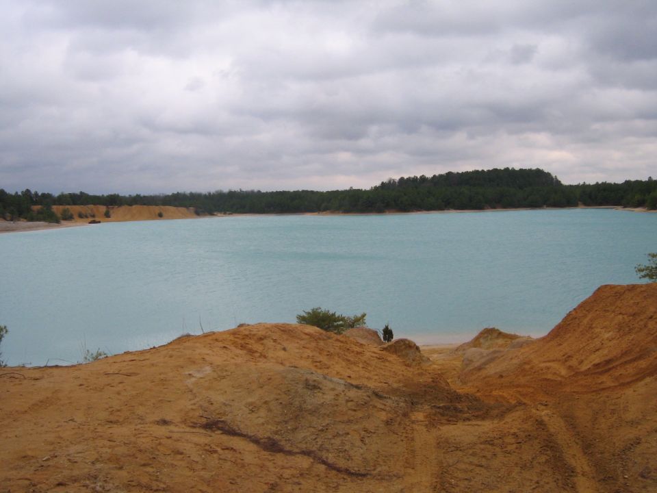 Turquoise lake with sandy shores and a forest under a cloudy sky.