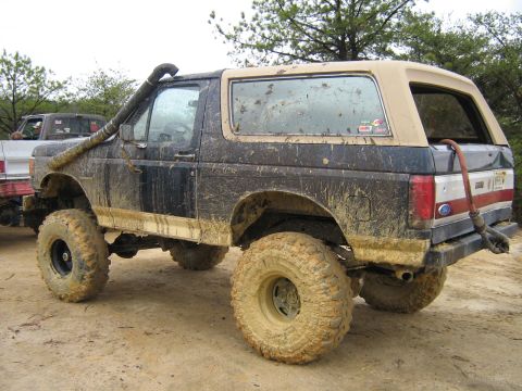1990 Ford Bronco - A heavily mud-covered black 1990 Ford Bronco is parked on a dirt road with large off-road tires and a snorkel intake visible. The vehicle h…