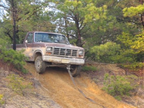 1990 Ford Bronco - A brown and tan pickup truck is stuck on a dirt hill with a tow strap attached to the front.