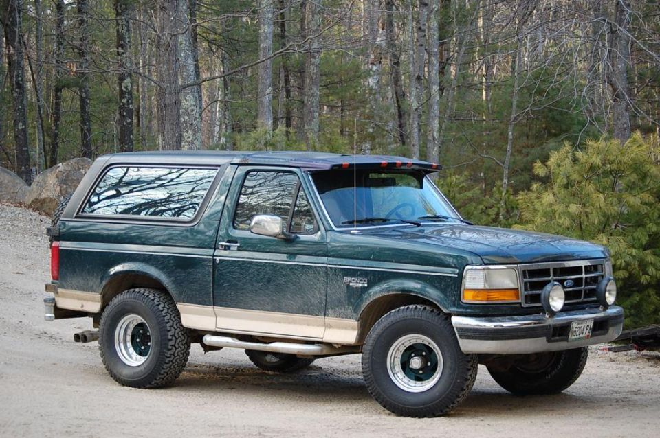 1993 Ford Bronco in dark green with tan trim, parked on a dirt road.