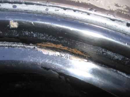 1993 Ford Bronco - Extreme close-up of a black-painted steel wheel's bead seat and rim flange, showing a patch of orange rust bleeding through the paint along…