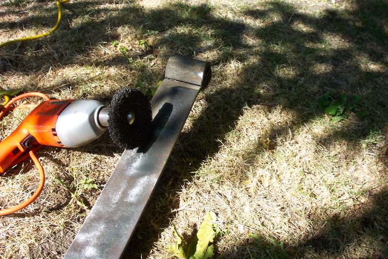 Angle grinder with abrasive wheel cleaning a steel bar on grass