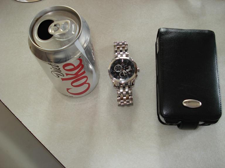 Diet Coke can, silver watch, and black phone case on a textured surface