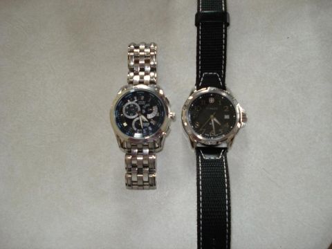2000 Ford Crown Victoria - Two watches are displayed on a textured surface. The watch on the left has a silver metal band and a black face with multiple subdials. The…