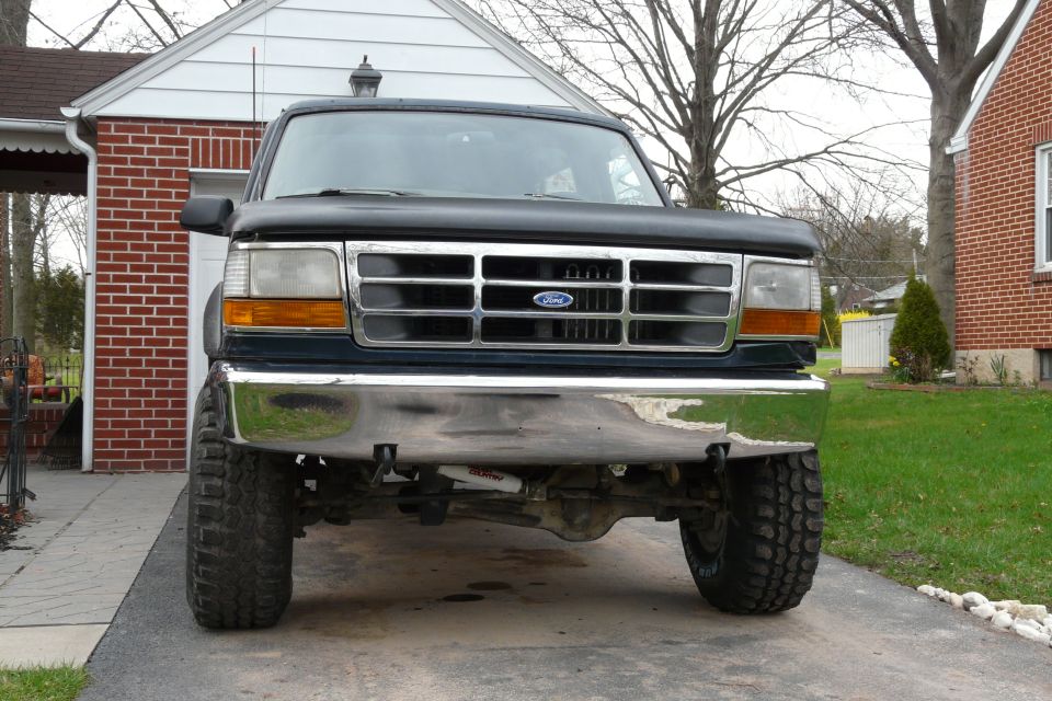 Front view of dark lifted Ford Bronco with chrome grille and big tires in a driveway