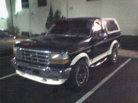 1993 Ford Bronco - A dark colored Ford Bronco is parked in a parking lot at night. The vehicle has a white top and white trim along the lower body.