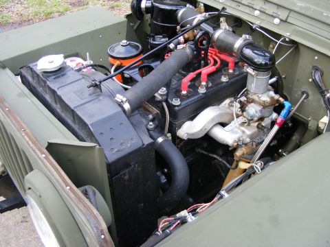 1979 Ford Bronco - Close-up view of the engine compartment of a vintage military-style vehicle, showing the radiator, engine block, carburetor, and associated…