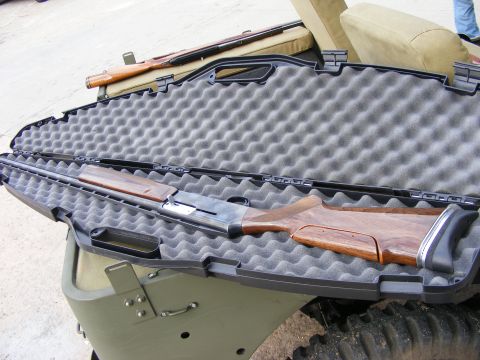 1979 Ford Bronco - A disassembled shotgun is laid out in a black foam-lined case, which rests on the olive green exterior of what appears to be a Ford Bronco.…