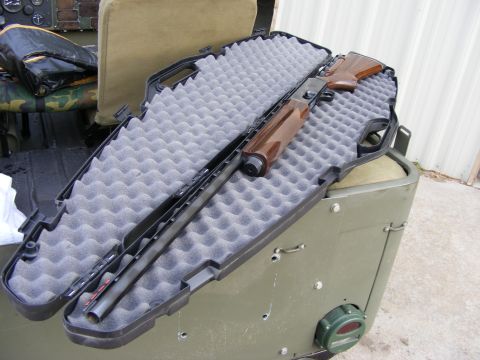 1979 Ford Bronco - A shotgun is placed in an open black gun case with gray foam padding. The gun case is resting on a green military-style vehicle.