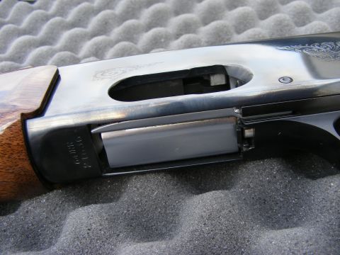 1979 Ford Bronco - A close-up, side view of the receiver and magazine well of a shotgun, resting on a gray foam surface. Engraved scrollwork is visible on the…