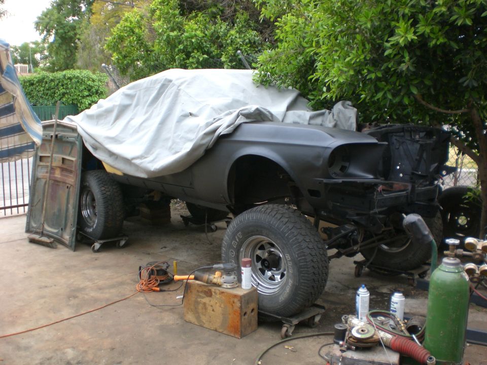 Classic car covered with a tarp, on dollies with off-road tires, tools and equipment nearby.