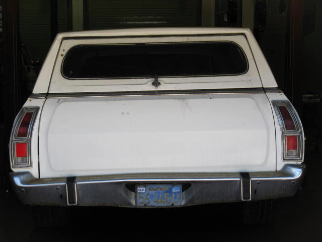 Rear view of a white 1973 Ford Ranchero with a camper shell and chrome bumper.