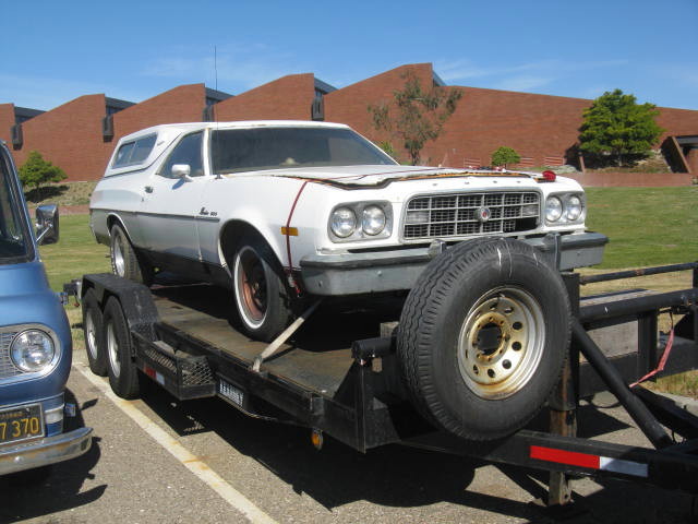 White coupe utility vehicle on a trailer next to a blue van