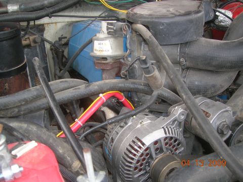1985 Ford Bronco - A close-up view of the engine bay of a Ford Bronco, focusing on the alternator and various hoses and electrical components. The image is da…