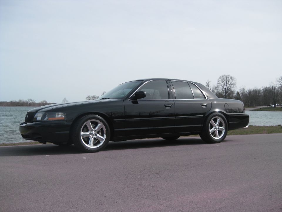Black four-door sedan with chrome wheels parked by a lake.